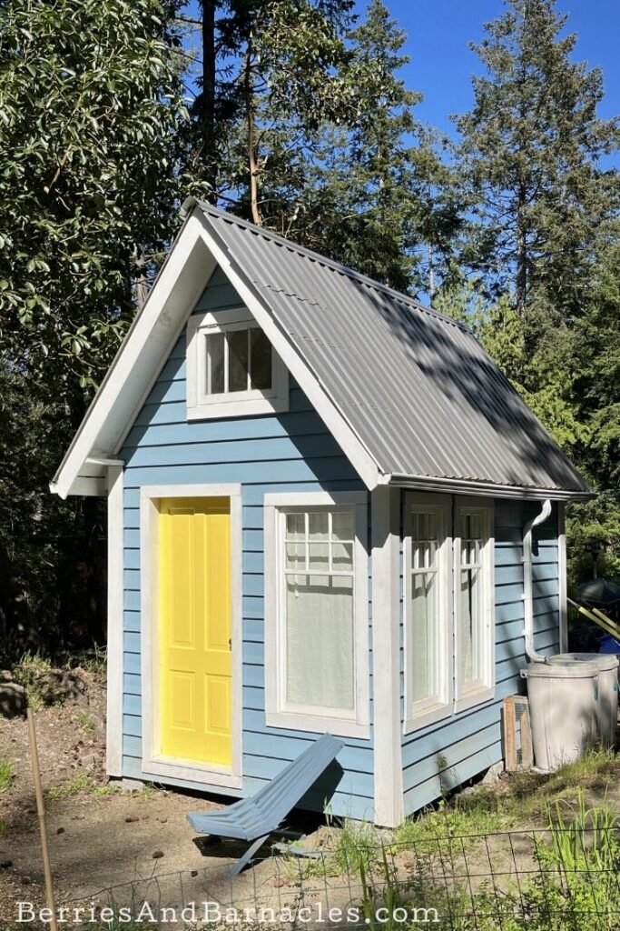 Bunkie or shabin building with a bright yellow door and blue clapboard sidding.