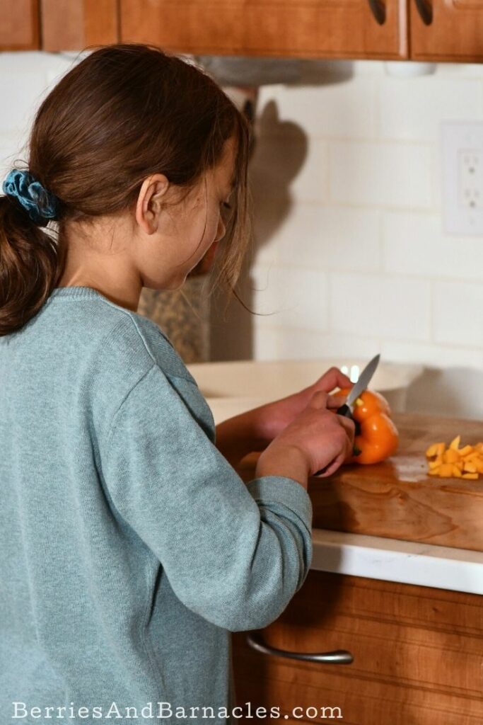 Child slicing an orange pepper.